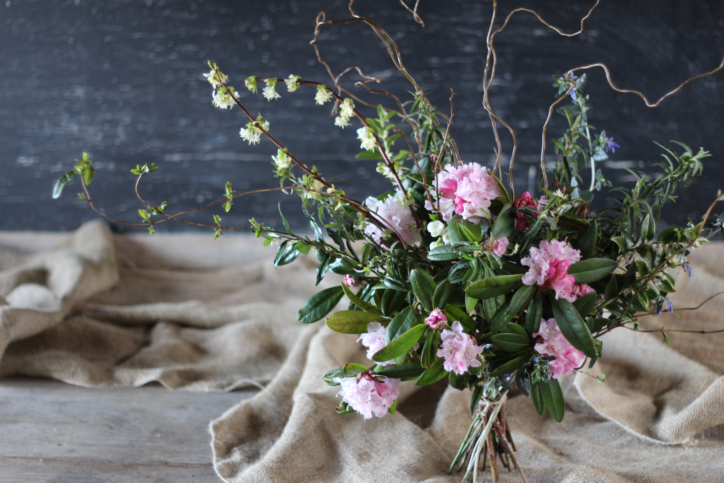 A wild looking bouquet of late winter flowering shrubs in pink and white by Ravenshill Flower Farm.